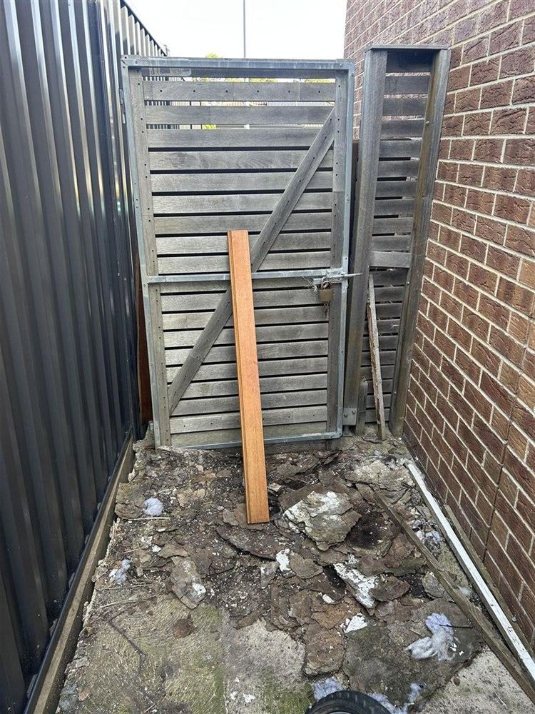 Weathered grey horizontal slat gate with debris and broken base before repair